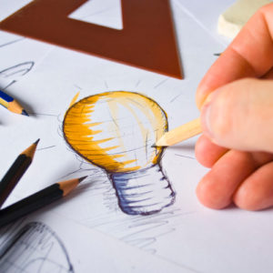 Uma mão desenhando com lápis uma lâmpada